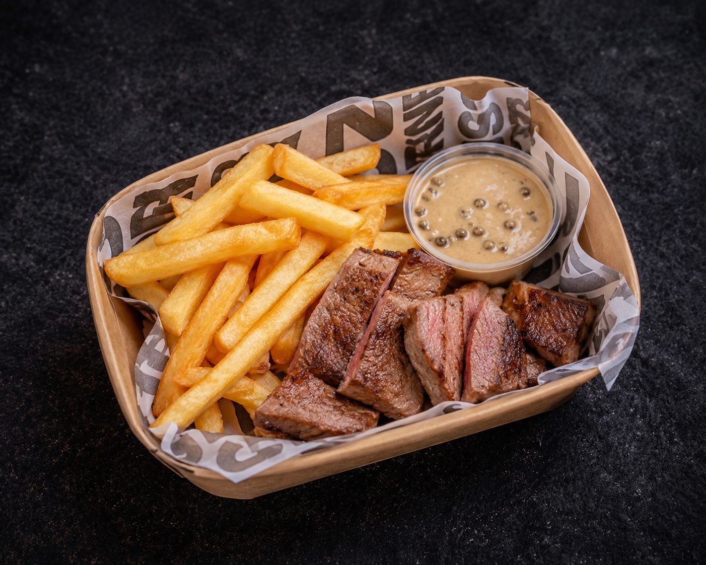Basket of fries and sliced meat with a dipping sauce on a dark background